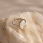 The Mother of Pearl Signet Ring in Sterling Silver, featuring a vintage-inspired round milky gemstone, is showcased on a creamy textured stone surface.