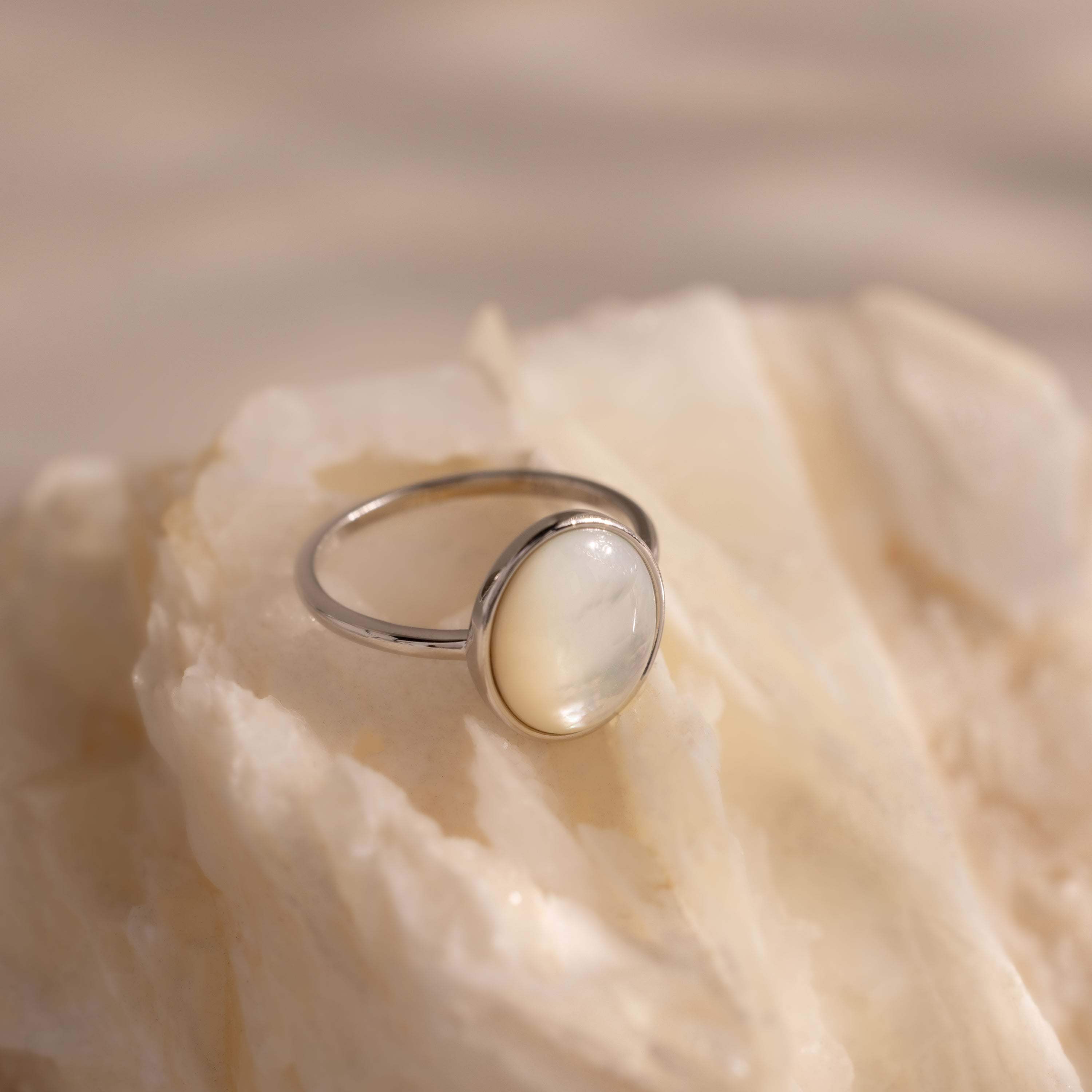 The Mother of Pearl Signet Ring in Sterling Silver, featuring a vintage-inspired round milky gemstone, is showcased on a creamy textured stone surface.