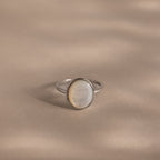 The Mother of Pearl Signet Ring in Sterling Silver features an oval, iridescent white mother-of-pearl stone set on a smooth, beige-toned surface.
