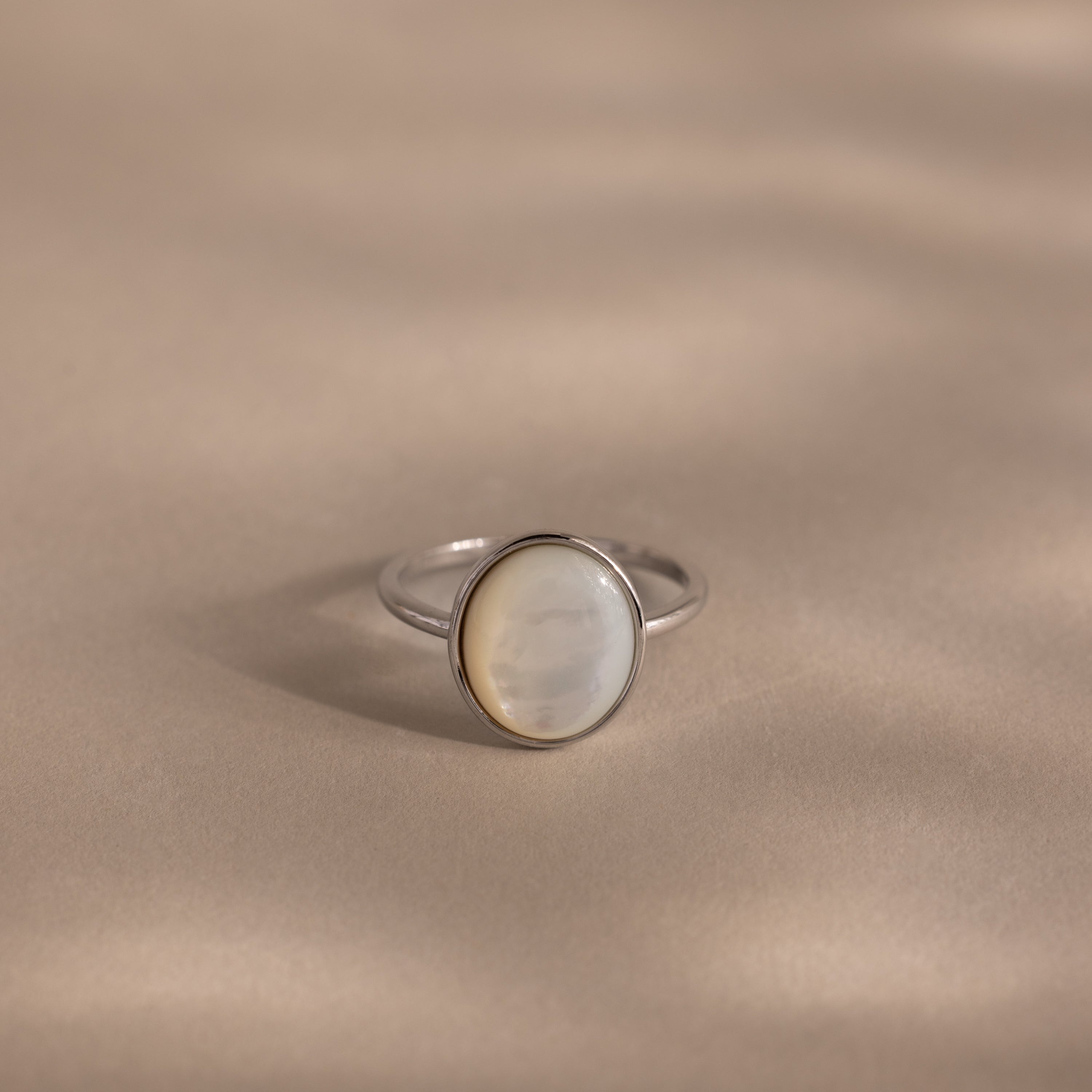 The Mother of Pearl Signet Ring in Sterling Silver features an oval, iridescent white mother-of-pearl stone set on a smooth, beige-toned surface.