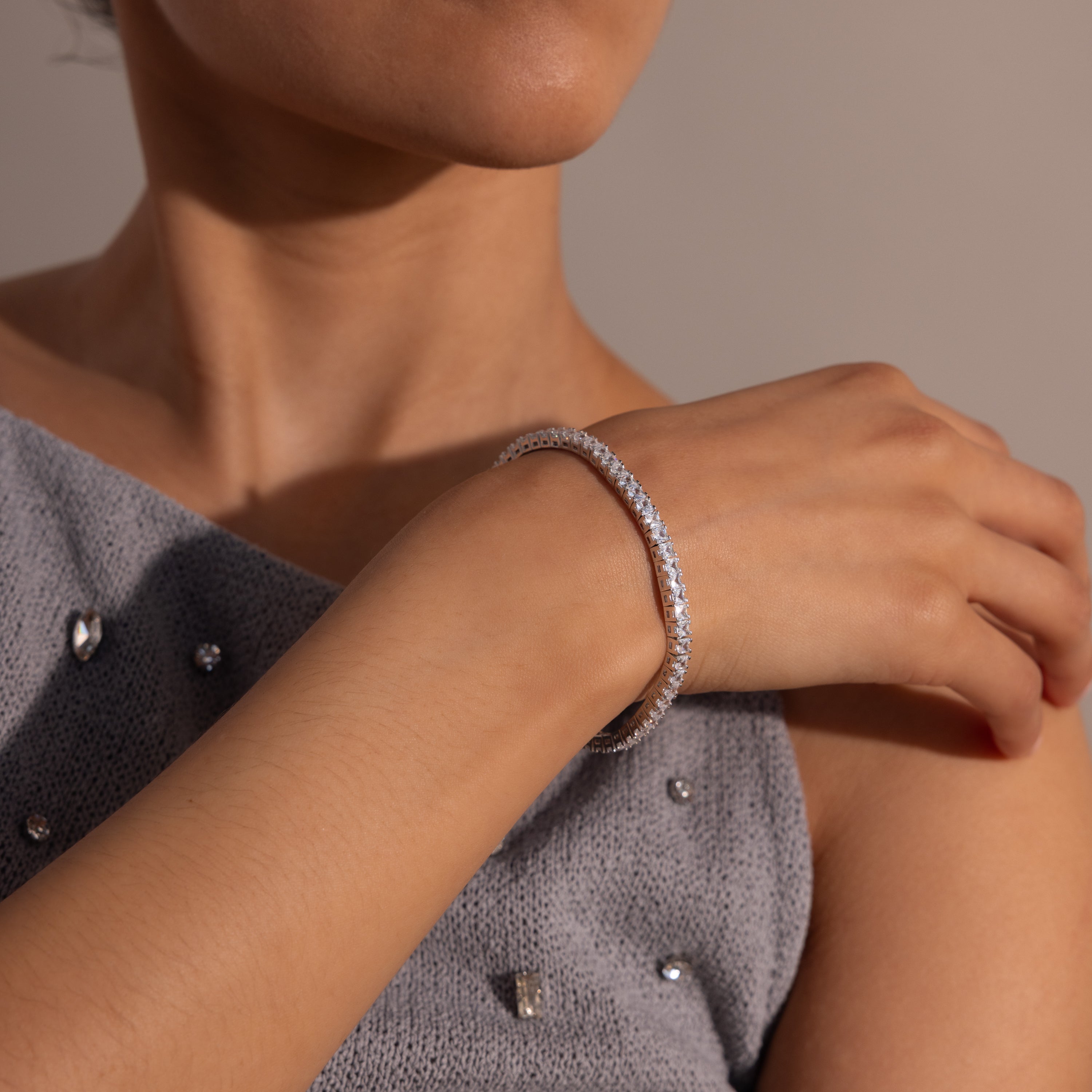 A woman wearing a Princess Diamond Tennis Bracelet in White Gold and a textured, sleeveless top with sparkling embellishments.