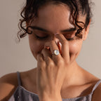 A woman smiles with her eyes closed, touching her nose, while wearing a vintage-inspired Mother of Pearl Signet Ring in Sterling Silver featuring a white stone.