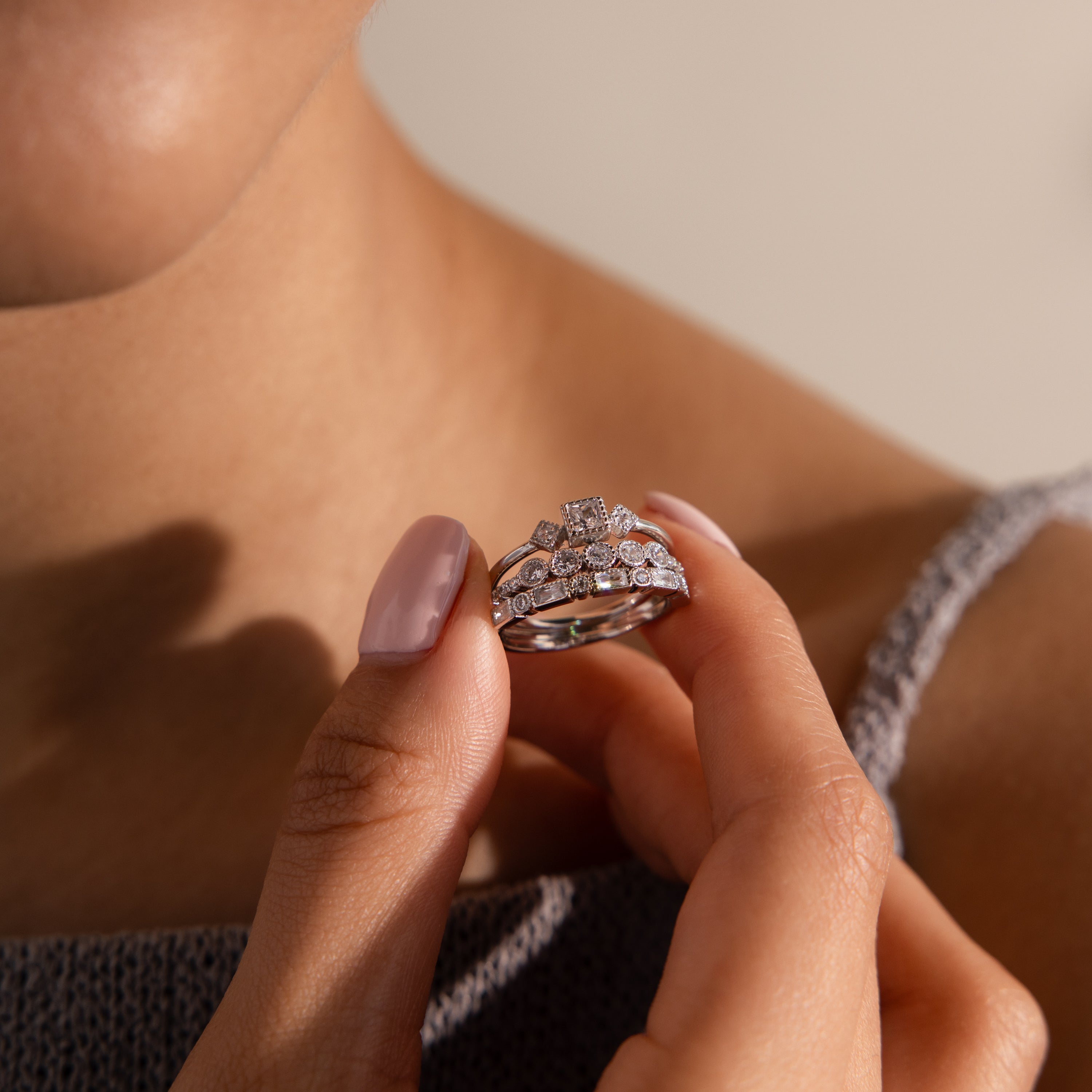 Dressed in a gray textured top, a person holds the Art Deco Diamond Ring Set near their chest, radiating vintage glamour.