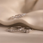 Three silver Art Deco rings with round, baguette, and square-cut diamonds displayed on soft, cream-colored fabric.