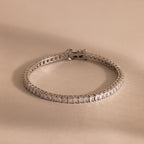 The Princess Diamond Tennis Bracelet, featuring sparkling princess-cut diamonds, is showcased on a beige background.