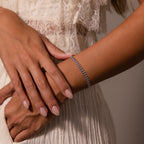 A woman wearing the Fishtail Chain Bracelet in Silver and a cream lace dress gently rests her hands on her arm.
