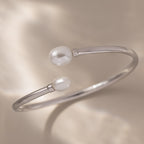 The Serenity Pearl Cuff Bracelet in Silver features radiant pearls on each open end, elegantly displayed against a soft beige background.