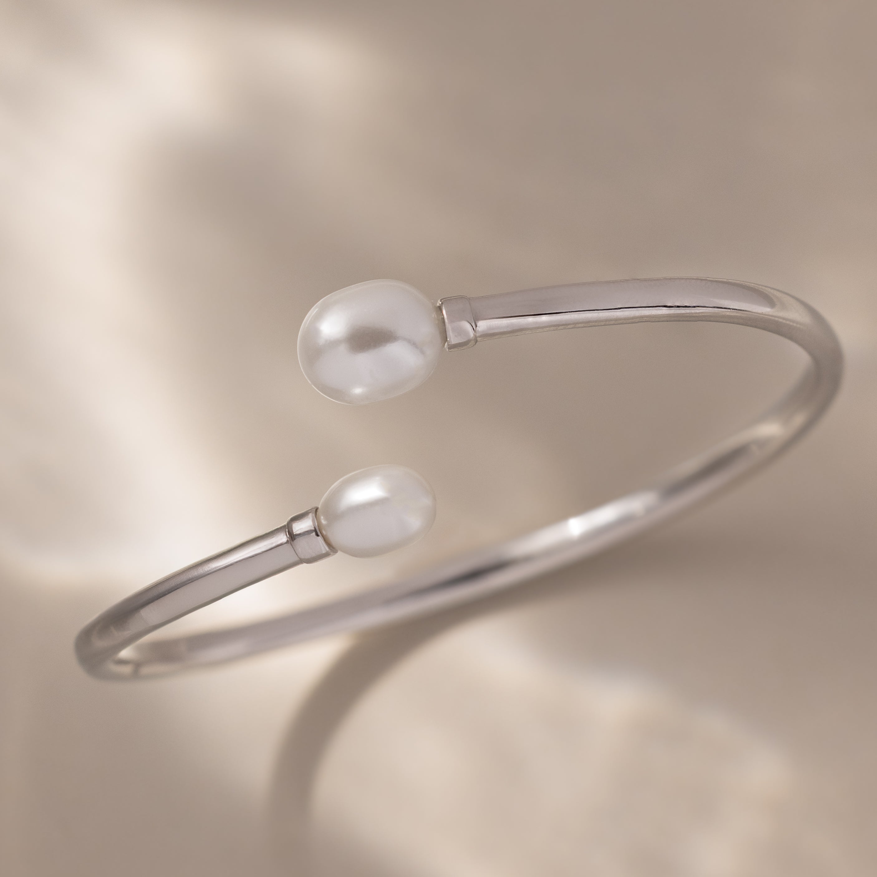 The Serenity Pearl Cuff Bracelet in Silver features radiant pearls on each open end, elegantly displayed against a soft beige background.