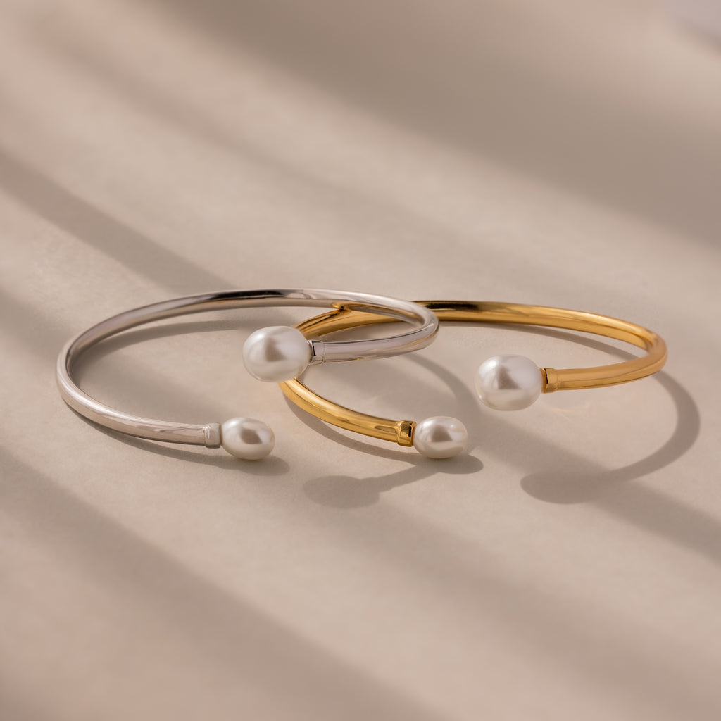 The Serenity Pearl Cuff Bracelet, available in silver and gold with pearls on each end, highlights modern pearl jewelry against a neutral background.