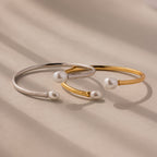 The Serenity Pearl Cuff Bracelet, available in silver and gold with pearls on each end, highlights modern pearl jewelry against a neutral background.