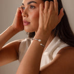 Woman adjusting her hair, wearing a sleeveless top and the Serenity Pearl Cuff Bracelet in Silver featuring a luminous open band design on her wrist.