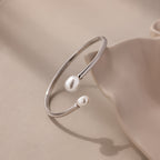 Serenity Pearl Cuff Bracelet: A silver open band bracelet featuring two white pearls, showcased on a soft beige surface.