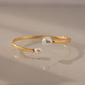 The Serenity Pearl Cuff Bracelet in 18K Gold features two white pearls on each end and a sleek open band, creating a modern and elegant jewelry piece.