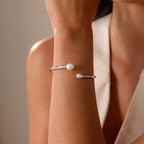 A woman wearing the Serenity Pearl Cuff Bracelet in Silver on her wrist, paired with a sleeveless white top.
