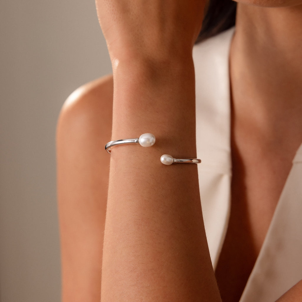 A woman in a sleeveless top wears the Serenity Pearl Cuff Bracelet, featuring two white pearls—a modern and elegant jewelry choice.