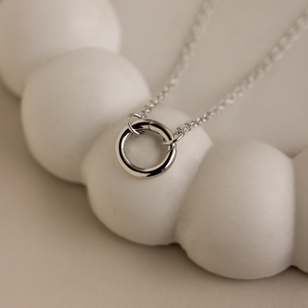 The Cable Circle Charm Necklace in Sterling Silver features a double pendant design, elegantly displayed on a rounded white surface—ideal for layering or as a standout charm necklace.
