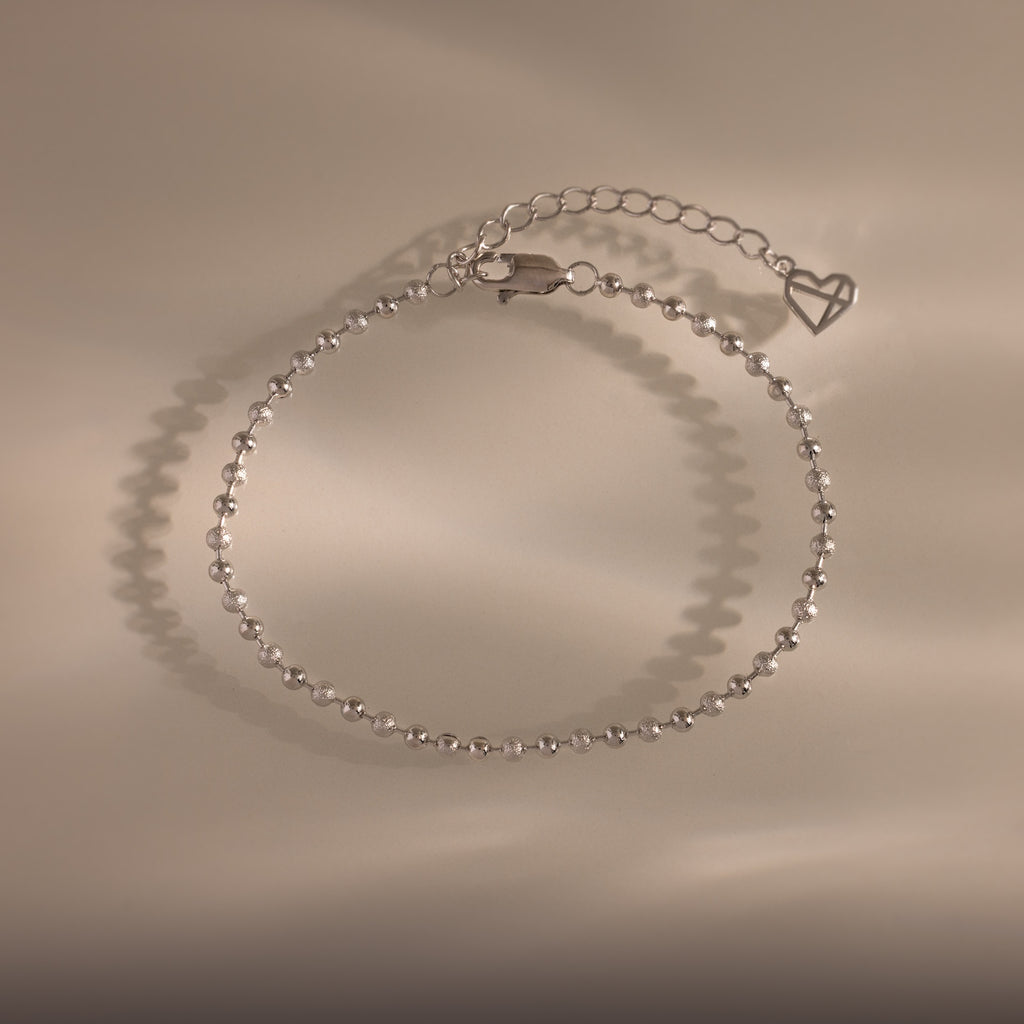 Dune Beaded Bracelet in Silver features polished silver beads, a heart charm, and an adjustable chain, displayed on a neutral background.