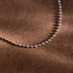 The Dune Beaded Bracelet in Silver rests on a textured brown surface, highlighted by soft shadows and warm lighting.