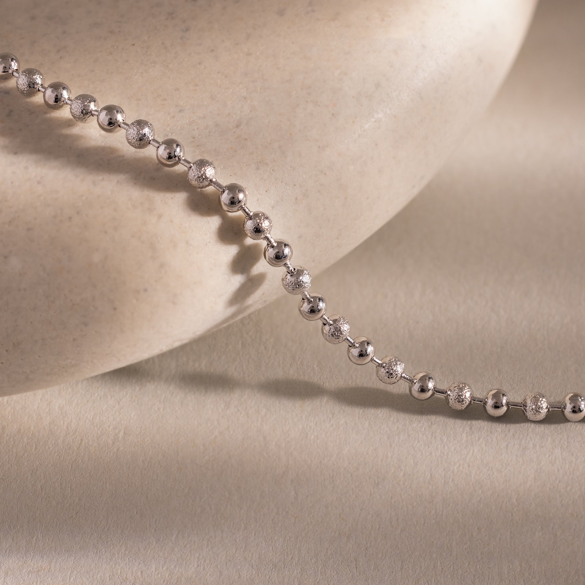 Close-up of the Dune Beaded Bracelet in Silver draped across a smooth, light stone surface, showcasing its polished silver beads.
