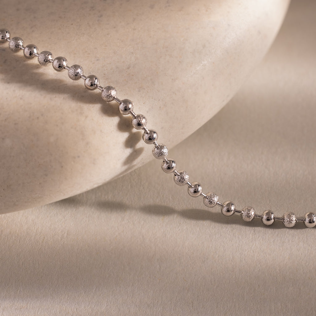 Close-up of the Dune Beaded Bracelet with polished silver beads resting on a smooth, beige stone surface.