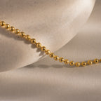 The Dune Beaded Bracelet, featuring gold beads and a layered design, is elegantly displayed draped over a smooth, light-colored stone on a neutral background.