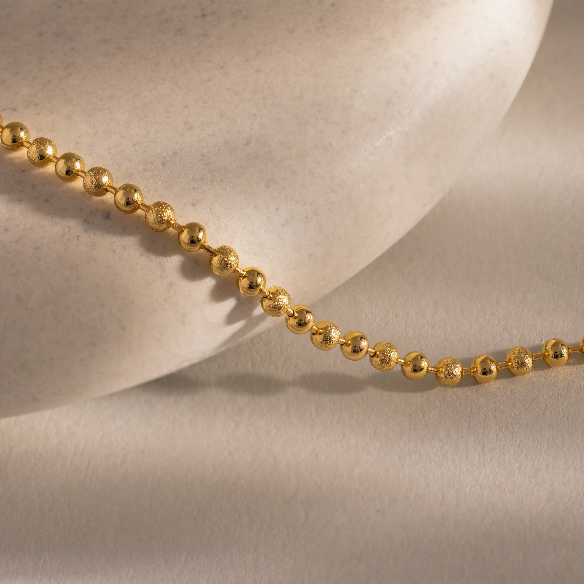 The Dune Beaded Bracelet, featuring gold beads and a layered design, is elegantly displayed draped over a smooth, light-colored stone on a neutral background.