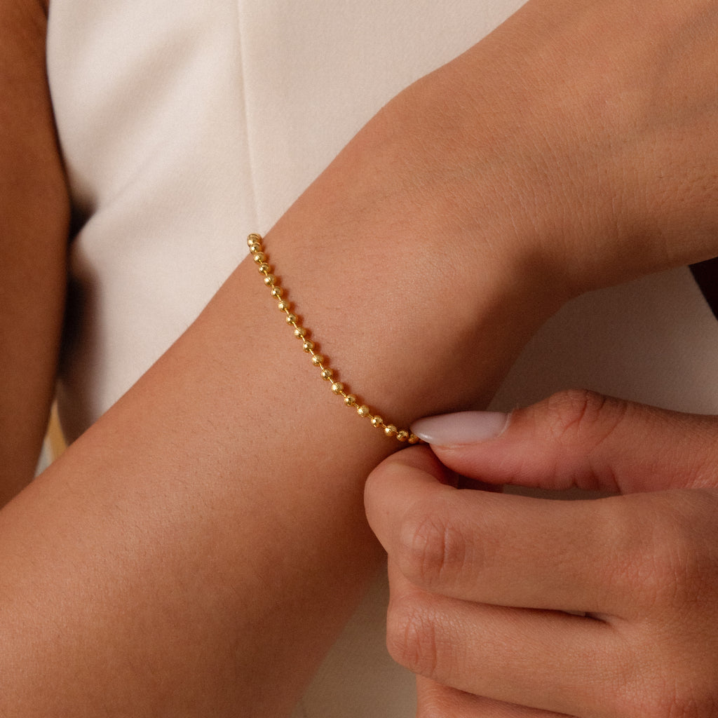 A person clasps a Dune Beaded Bracelet, featuring a delicate gold polished finish, around their wrist.