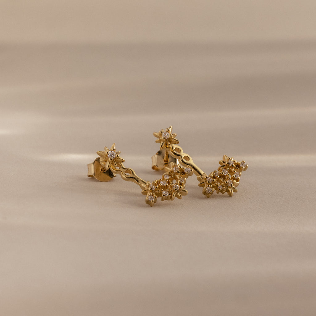 Starburst Cluster Ear Jackets in 18K Gold with small sparkling stones displayed on a soft beige surface.