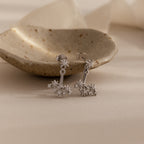 Starburst Cluster Ear Jackets in Sterling Silver, inspired by constellation designs, are displayed on a speckled ceramic dish with a soft beige background and gentle lighting.