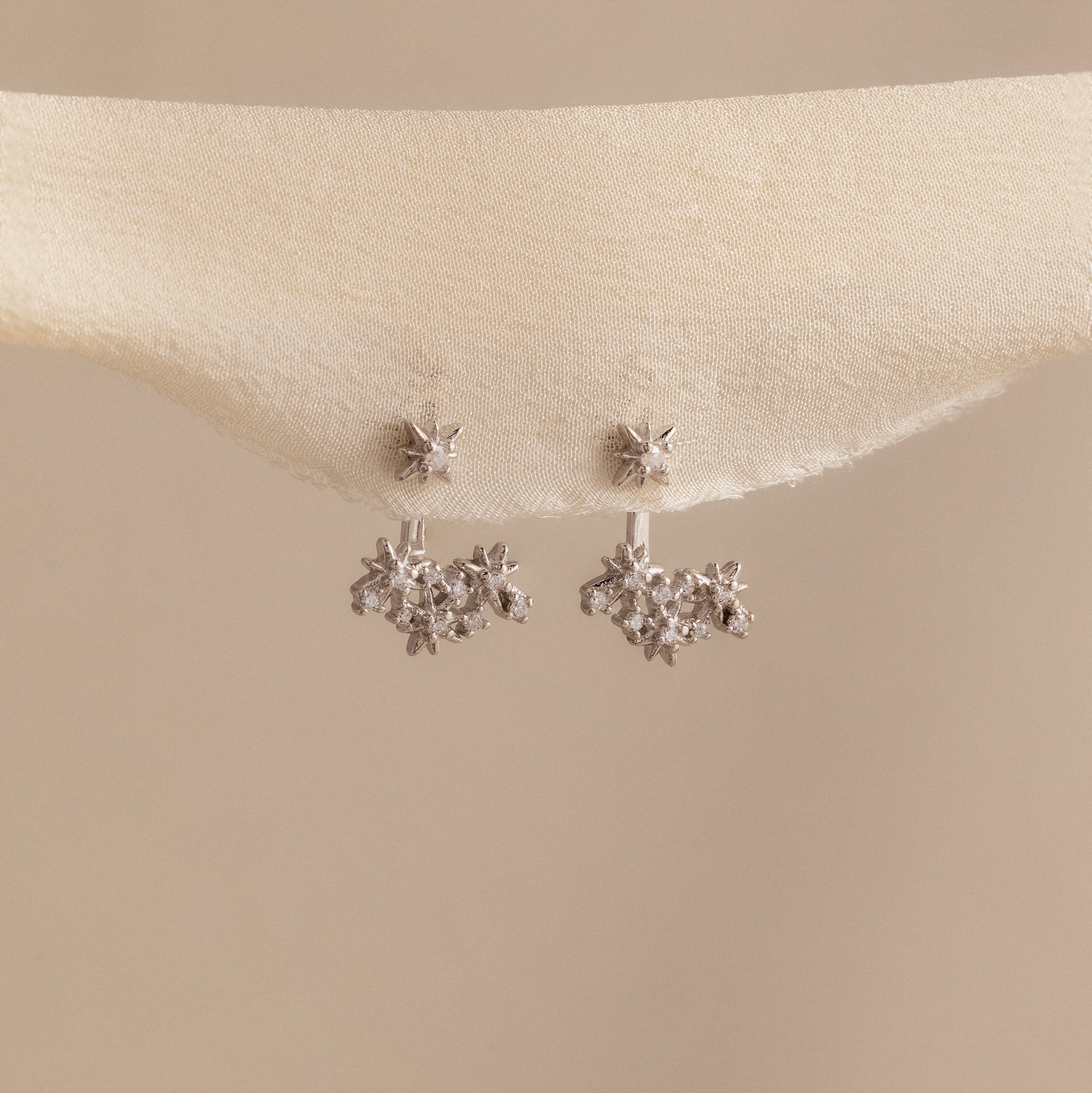 Starburst Cluster Ear Jackets in Sterling Silver, inspired by constellation earrings, displayed on a soft beige fabric background.
