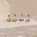 Four pairs of Starburst Cluster Ear Jackets, inspired by celestial jewelry and constellation designs, shimmer in gold and silver on a textured beige surface.