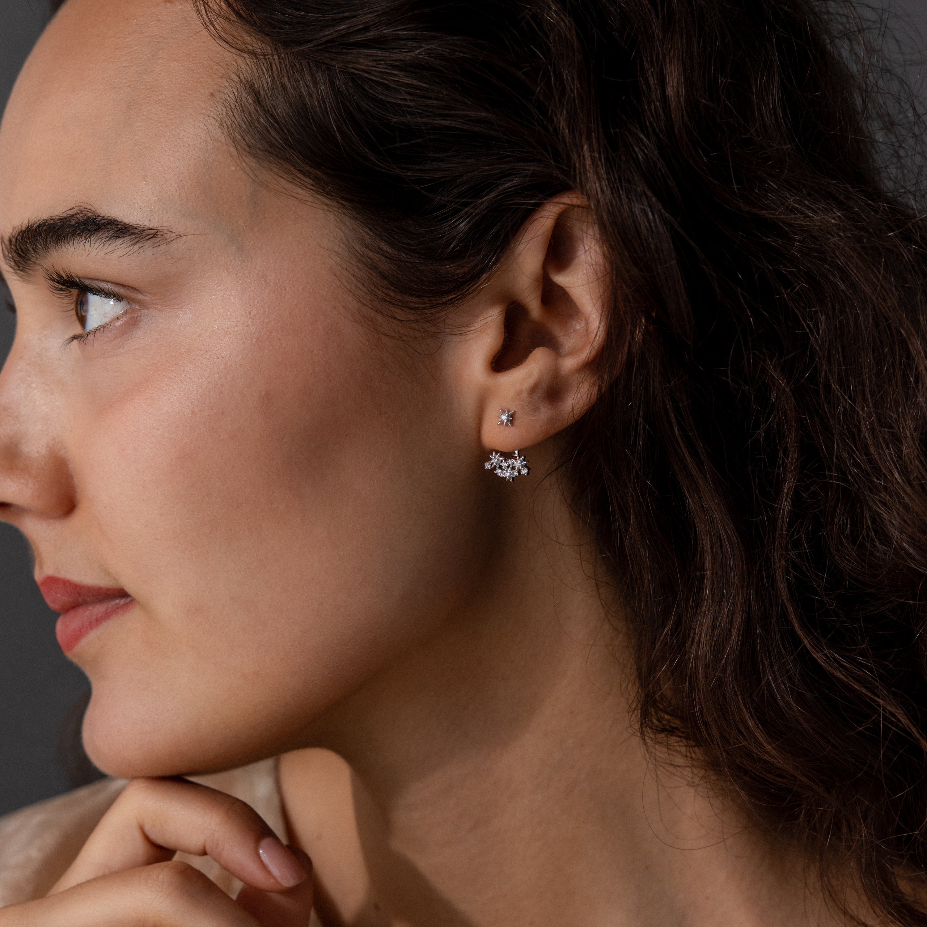 Woman with wavy brown hair wearing Starburst Cluster Ear Jackets in Sterling Silver, gazing thoughtfully to the left.