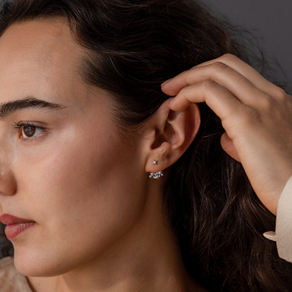 A woman with wavy dark hair touches her ear, showcasing Starburst Cluster Ear Jackets that capture the beauty of celestial jewelry.
