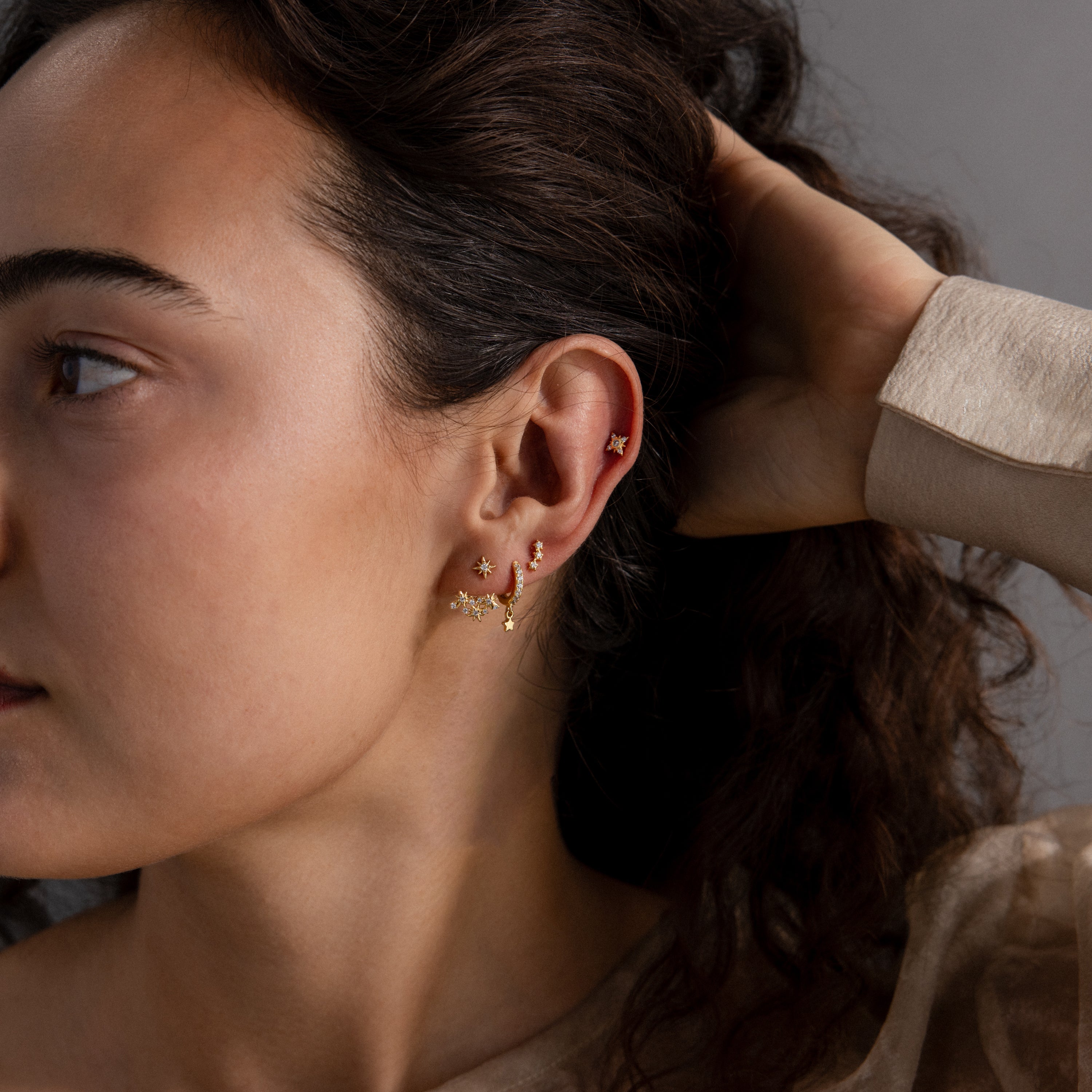 Woman with dark hair wearing Starburst Cluster Ear Jackets and multiple gold studs in her left ear, shown in profile against a neutral background.