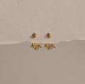 The Starburst Cluster Ear Jackets are displayed on a textured beige background, making them a perfect choice for fans of celestial jewelry.