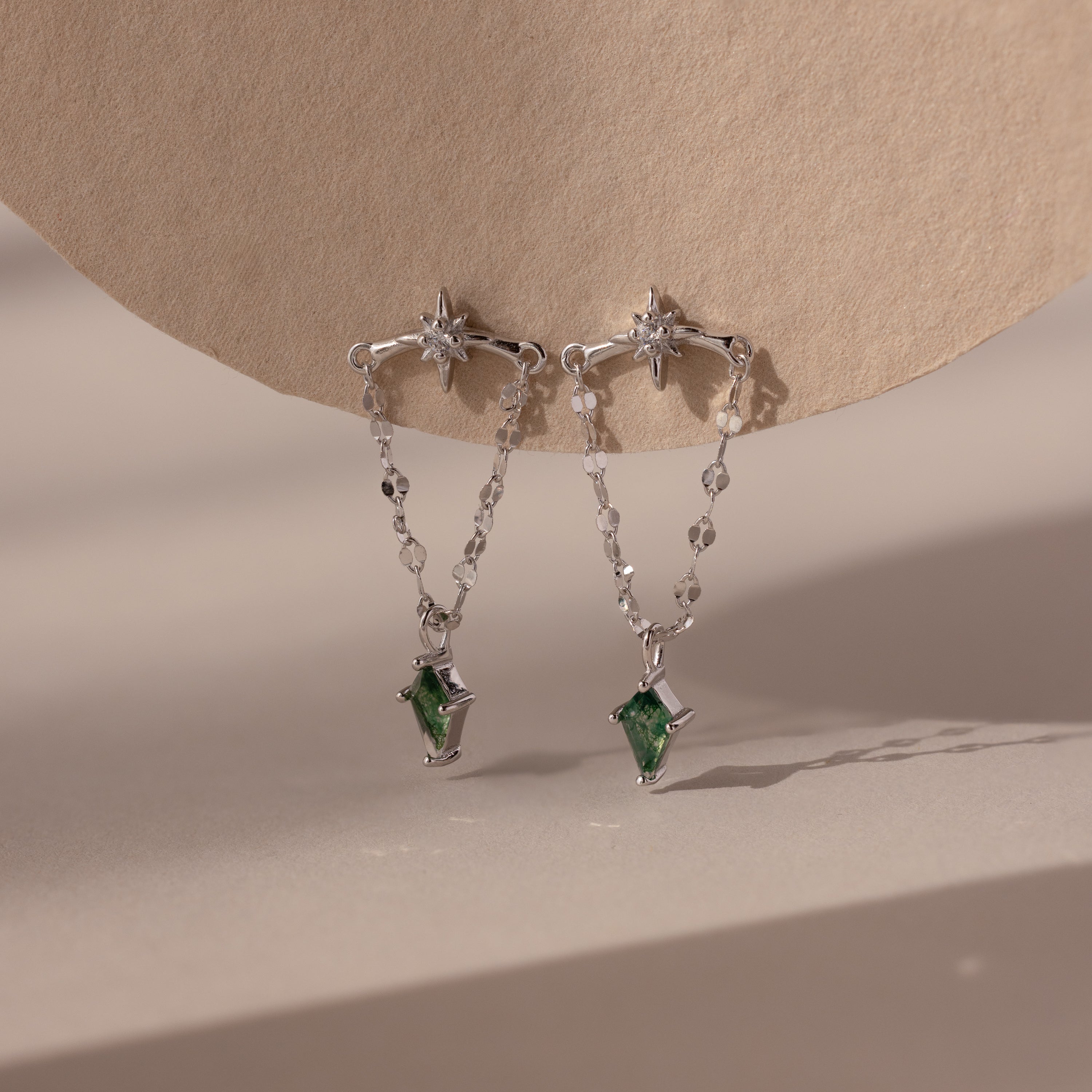 Agate Star Chain Earrings in Sterling Silver feature star-shaped studs, chain drops, and green agate gemstone pendants for a celestial look that dazzles against any neutral backdrop.