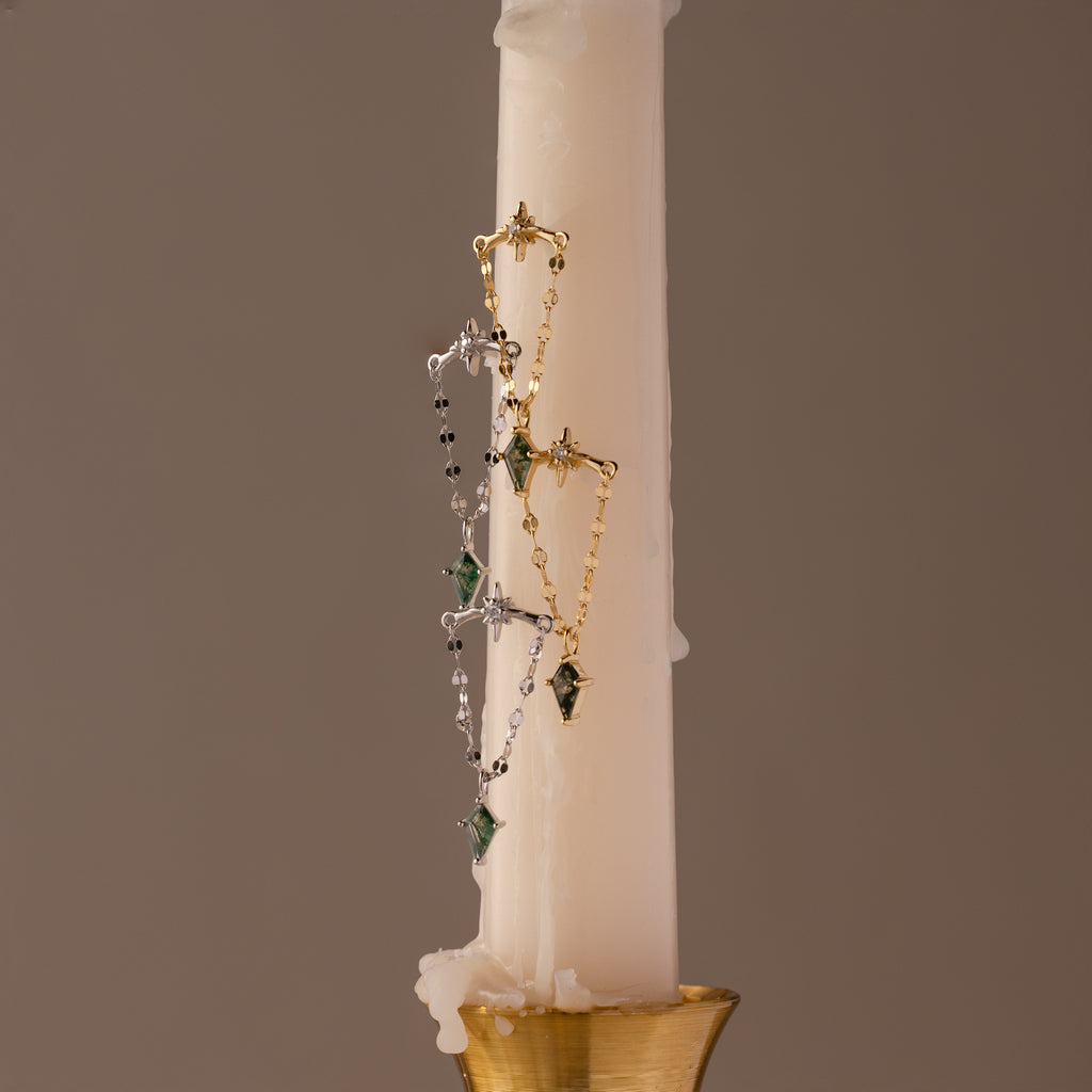 Gold and silver necklaces with green agate gemstones drape over a white candle in a gold holder, paired with Agate Star Chain Earrings in Sterling Silver for a celestial accent.