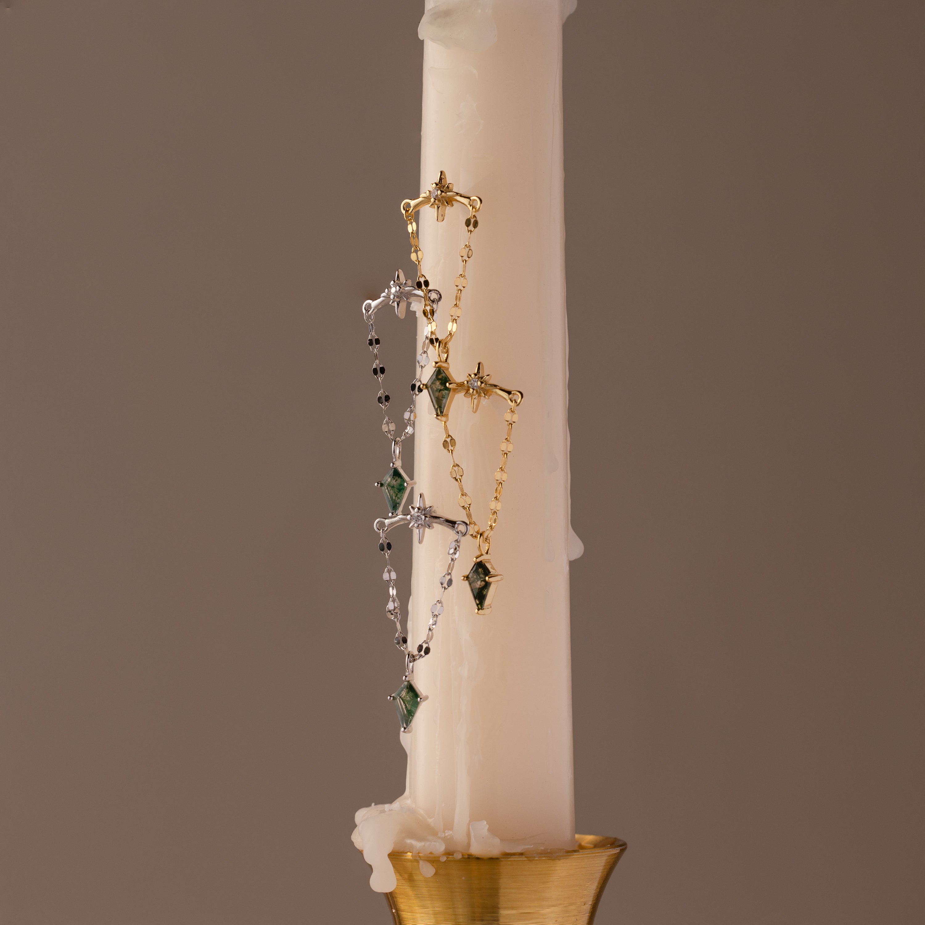 Gold and silver necklaces with green agate gemstones drape over a white candle in a gold holder, paired with Agate Star Chain Earrings in Sterling Silver for a celestial accent.