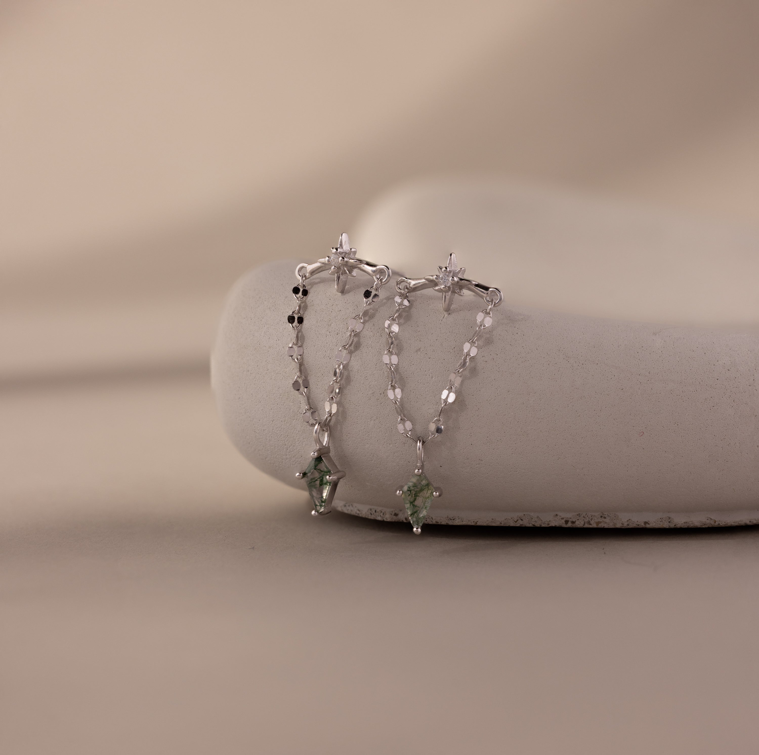 Agate Star Chain Earrings with silver dangle design and green agate star charms are displayed on a smooth white surface against a neutral background.