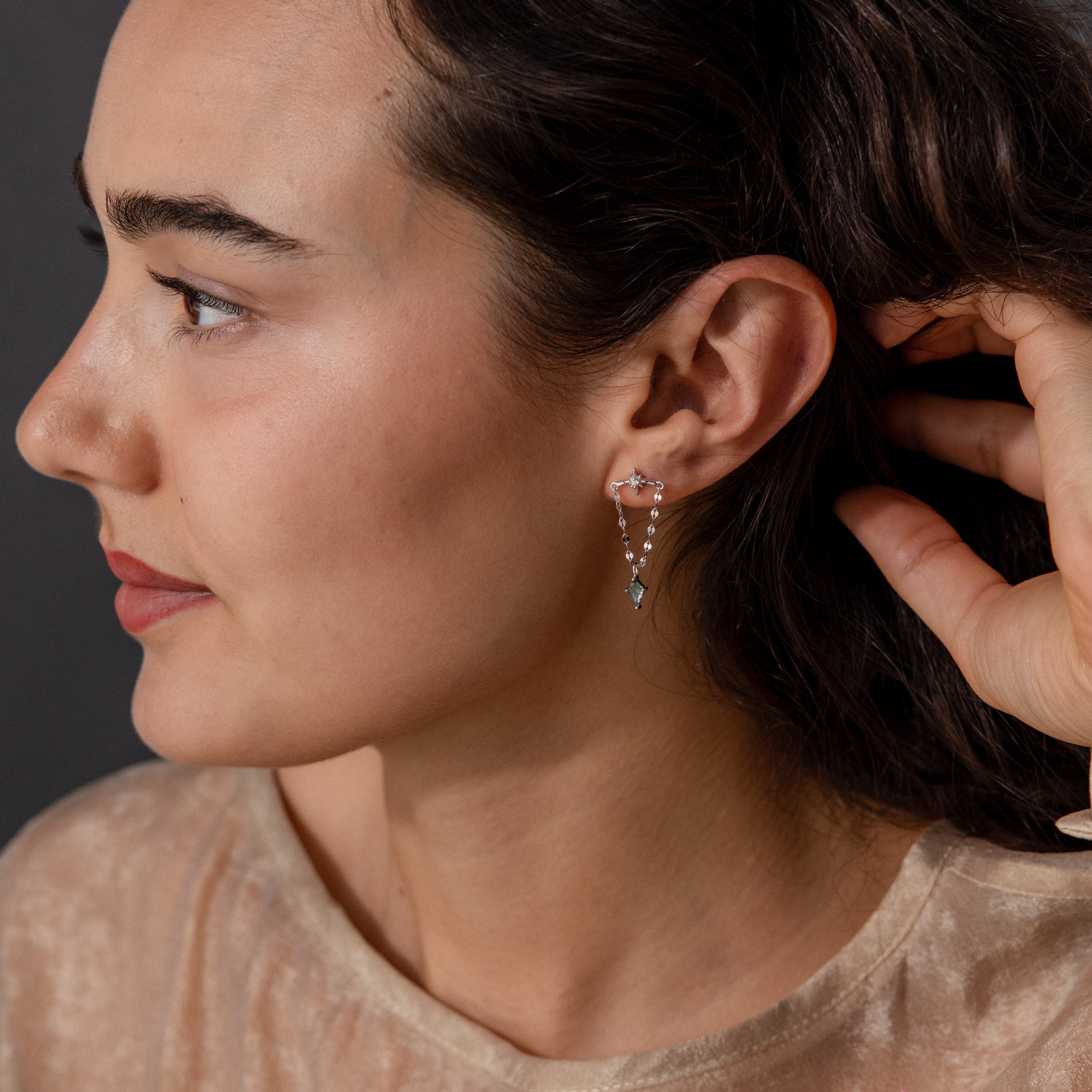 Woman with dark hair wearing a beige top and Agate Star Chain Earrings featuring delicate celestial details with small hanging gems, facing left.