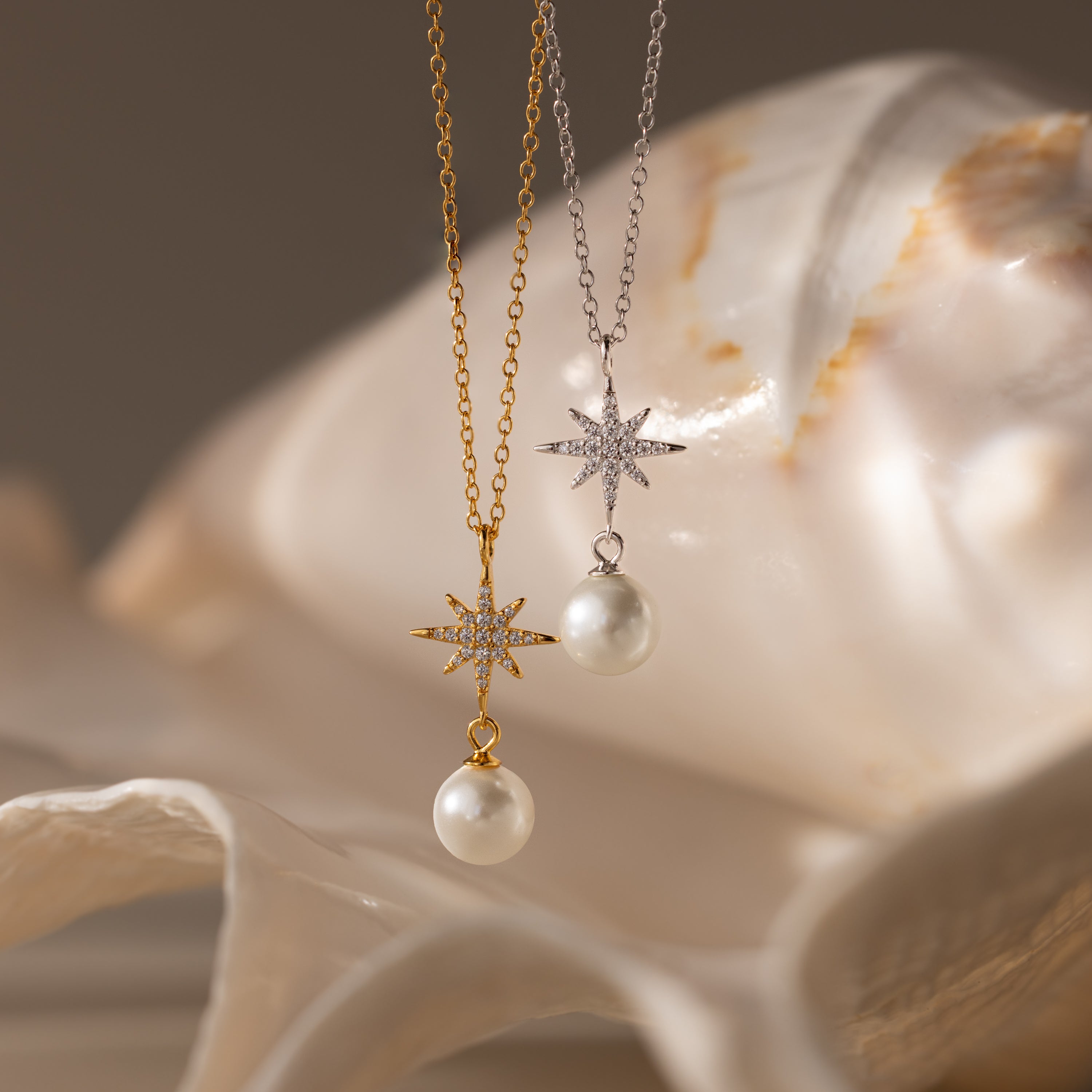 The North Star Pearl Necklace, available in gold or silver and adorned with pearls, is displayed against a seashell backdrop, highlighting its celestial elegance and unique design.