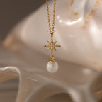 North Star Pearl Necklace in 18K Gold features a star-shaped pendant with sparkling diamonds and a dangling pearl, elegantly displayed on a white seashell—a stunning piece for any pearl jewelry collection.