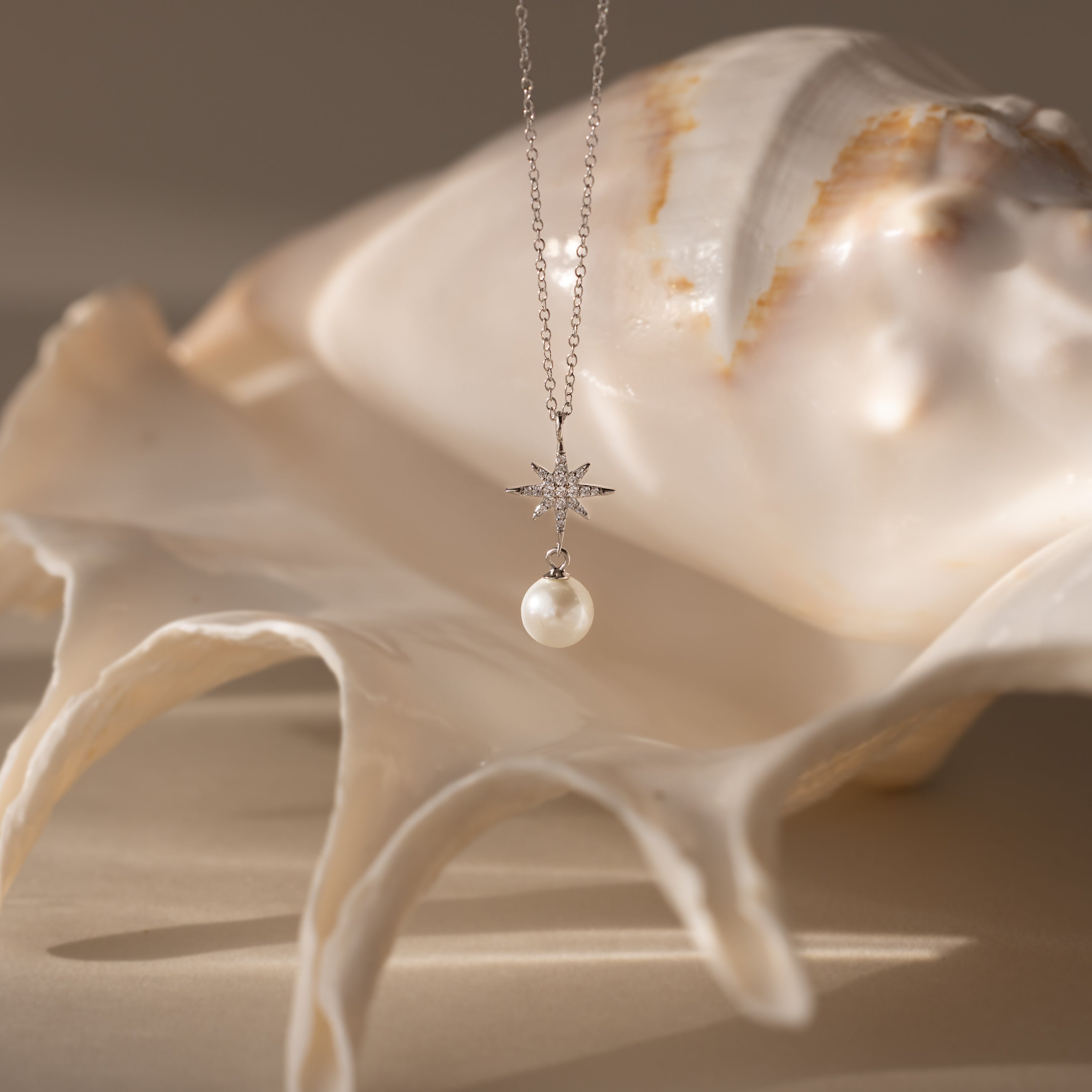 The North Star Pearl Necklace in Sterling Silver is displayed on a large white seashell, glowing softly in natural light.