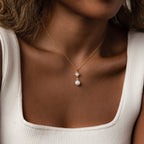 A woman wears the North Star Pearl Necklace in 18K Gold, a gold star pendant with a pearl, styled with a white square-neck top.