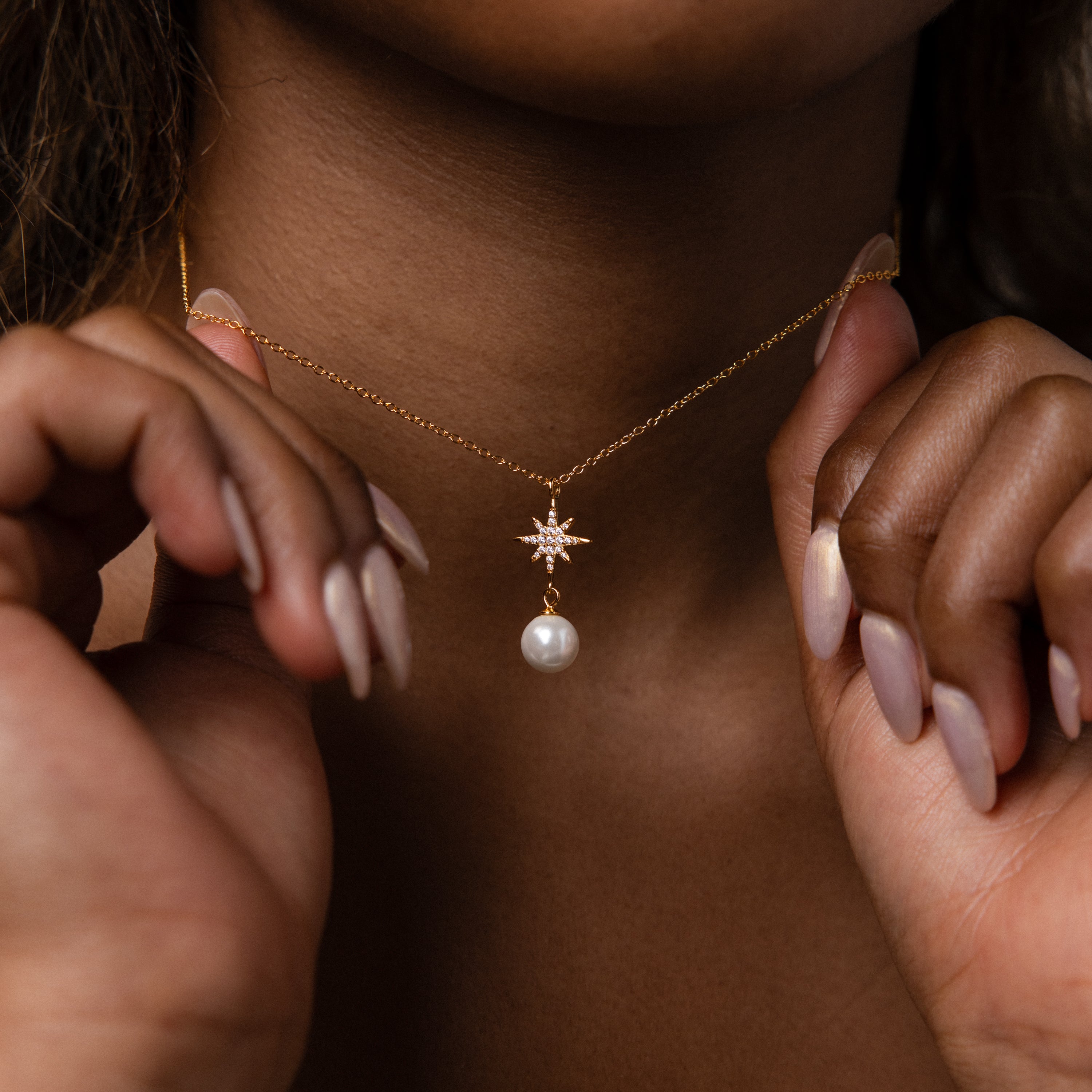 A woman displays manicured nails while holding the North Star Pearl Necklace, featuring a star pendant with a dangling pearl.