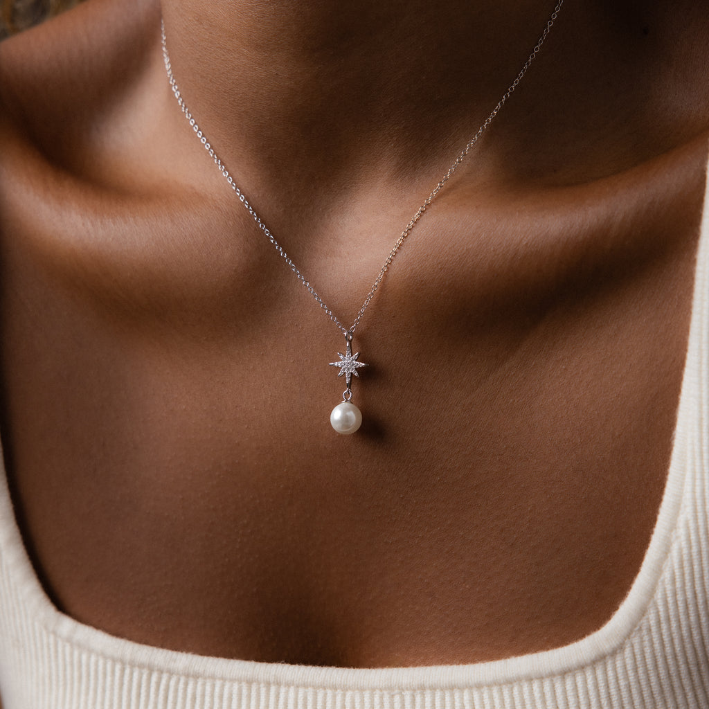 A woman wears the North Star Pearl Necklace in Sterling Silver, featuring a star-shaped setting and pearl, displayed against her collarbone and a cream top.