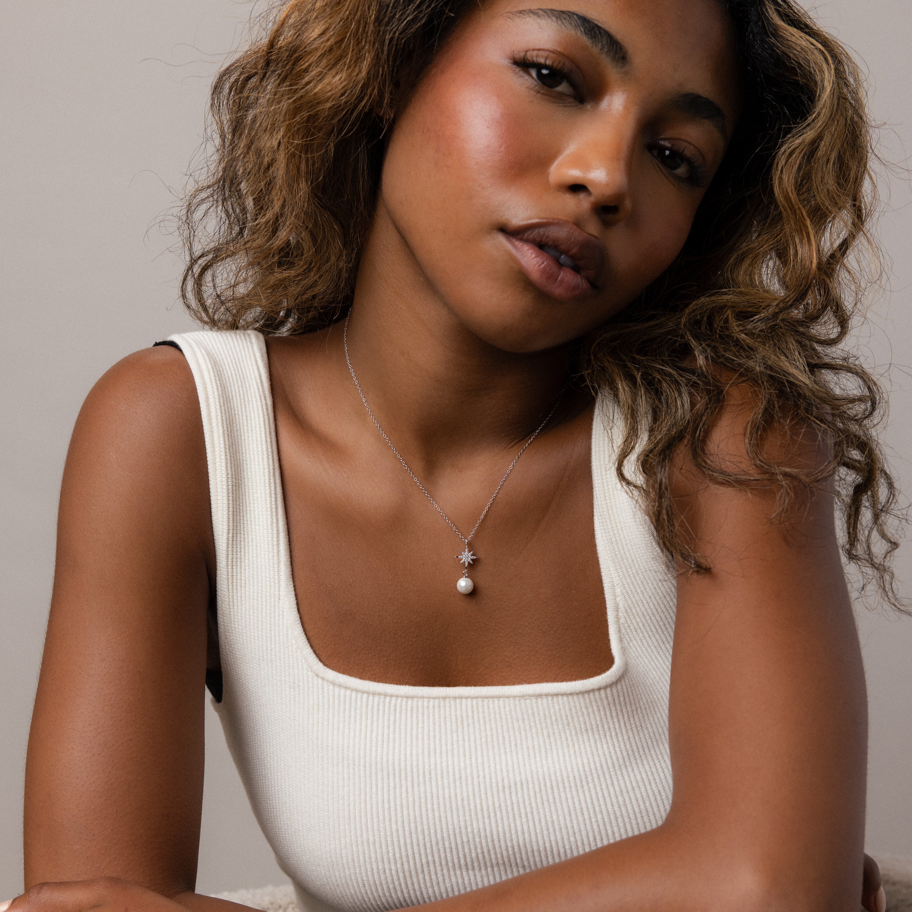Woman with wavy hair in a white tank top wears the North Star Pearl Necklace in Sterling Silver, featuring a delicate star pendant, while looking at the camera.
