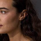 A woman with wavy brown hair wears Agate Diamond Dangle Earrings in Sterling Silver, shown in a close-up side profile to highlight their shimmering detail.