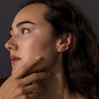 Woman with long dark hair looks left, touching her face, wearing Agate Diamond Dangle Earrings in Sterling Silver against a dark background.