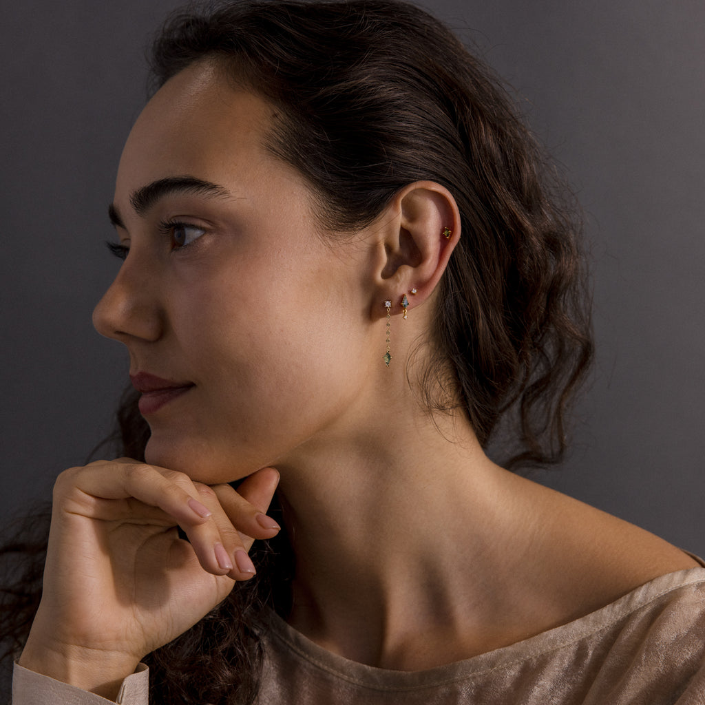 Woman with long brown hair looking left, wearing Agate Diamond Dangle Earrings in 18K Gold and a beige top, her hand resting thoughtfully on her chin.
